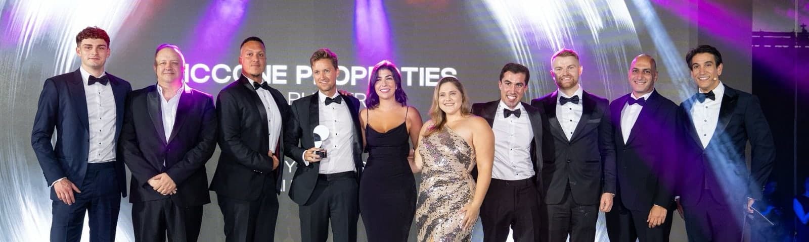 Eleven of the McCone Properties team in black tie on stage at the Property Finder Awards, one of them holding the award