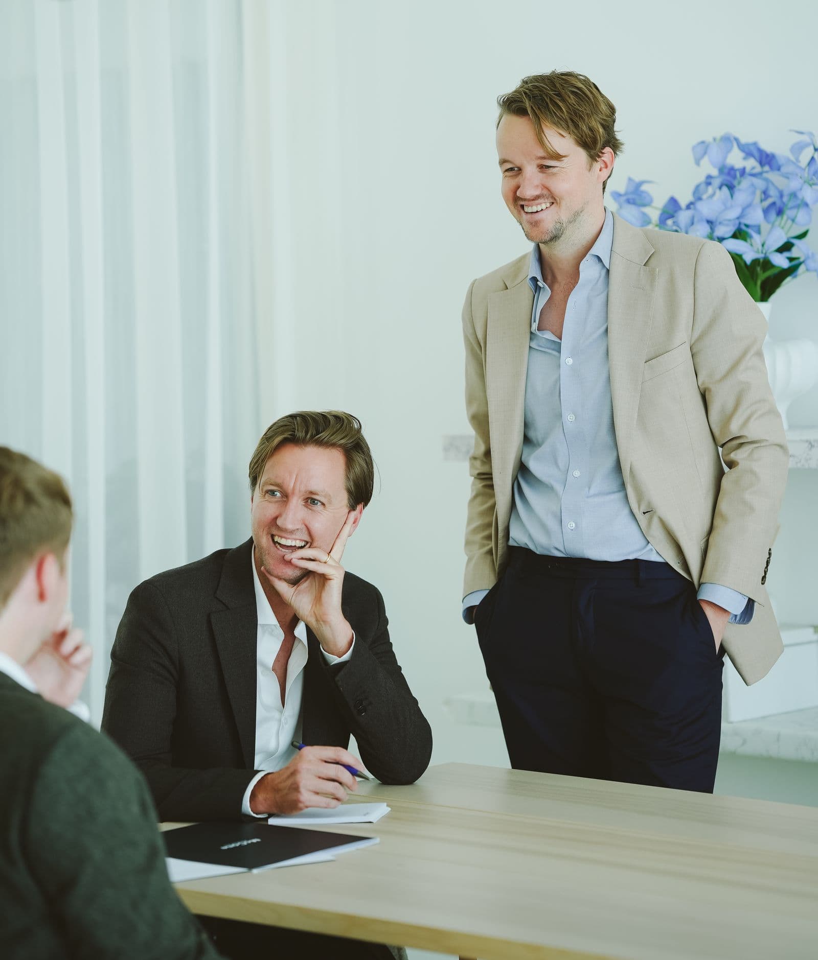 Two of the McCone Properties team laughing with a client across a meeting table in the office.