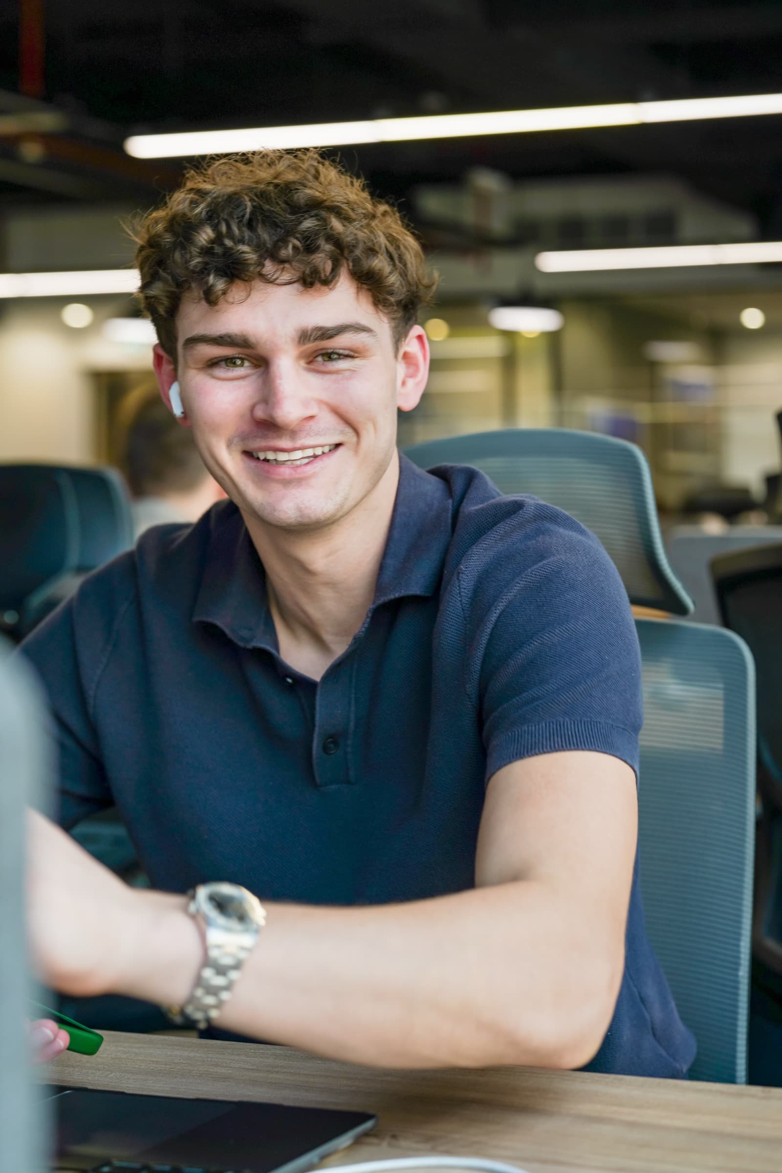 A McCone Properties agent smiling at his desk on the open office floor in The Greens, laptop open in front of him.