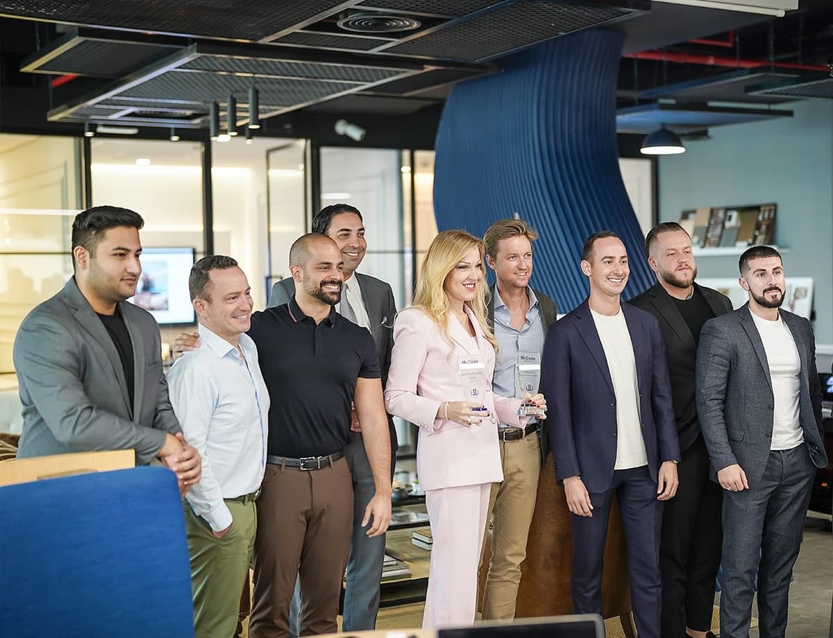 Nine members of the McCone Properties team standing together and smiling in the office, two of them holding glass awards.