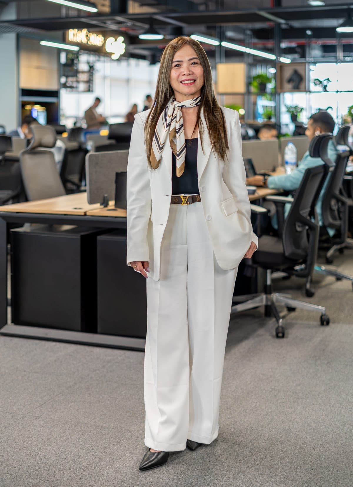 A McCone Properties agent in a white suit standing on the open office floor, colleagues at the desks behind her.