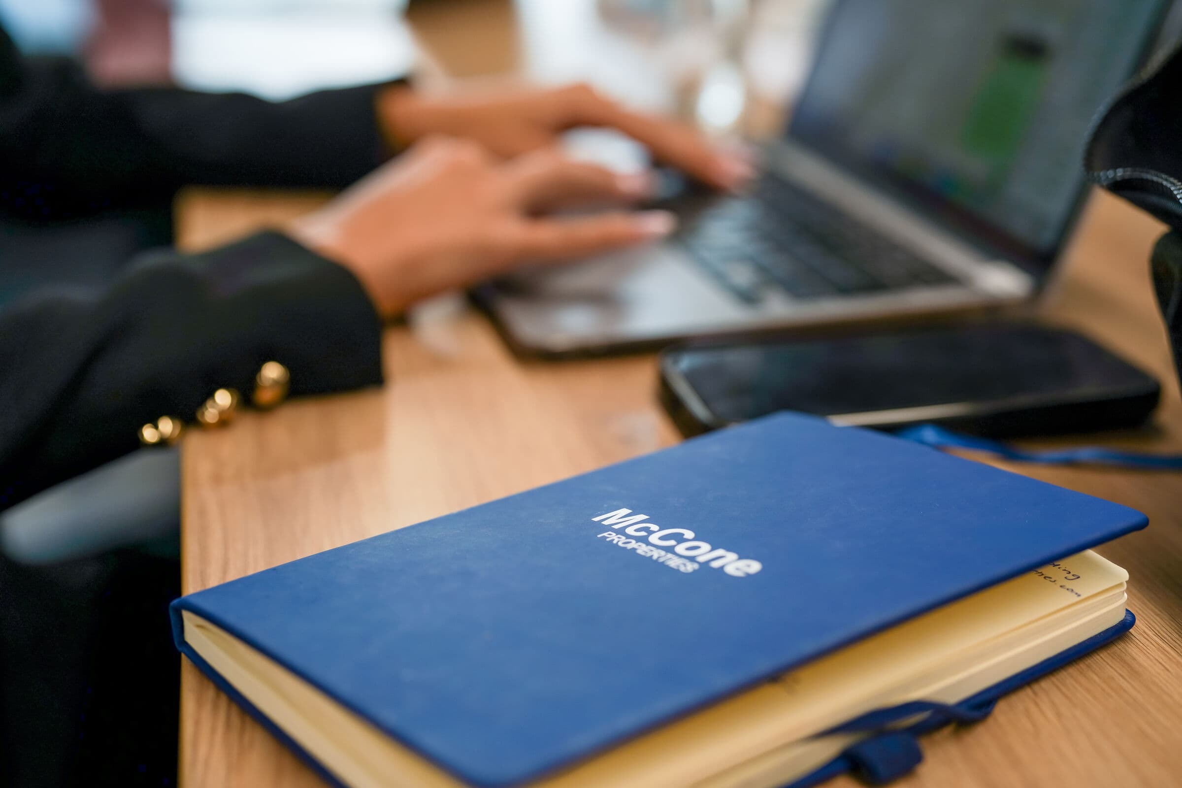A McCone Properties notebook on a desk beside a phone, with an agent typing on a laptop behind it