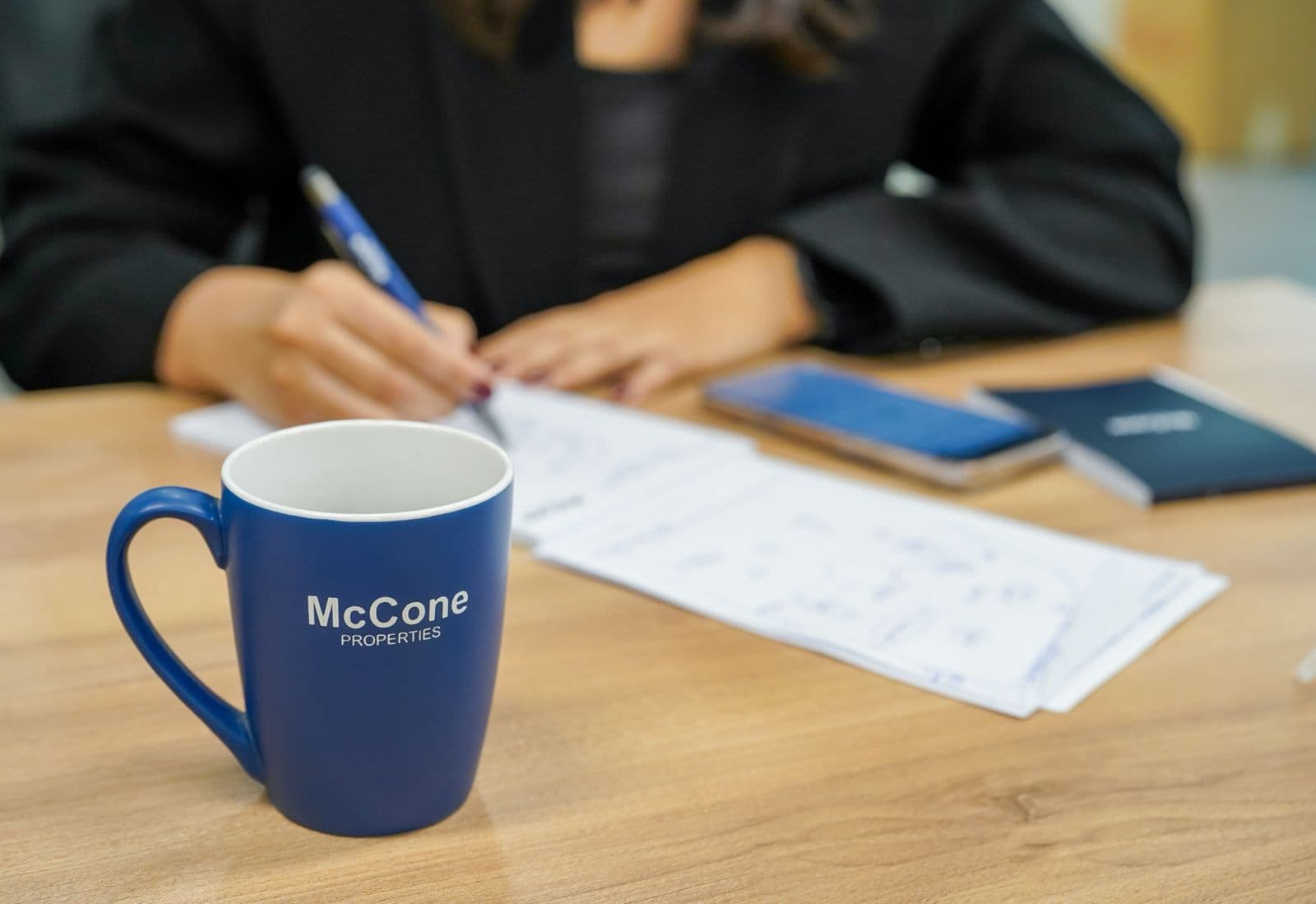 A McCone Properties mug on a desk while an agent works through printed figures with a pen behind it