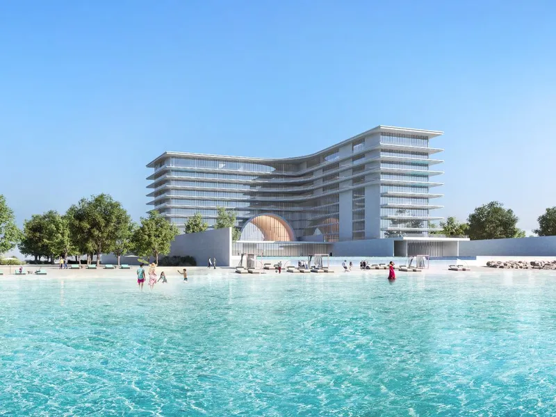 Curved terraced building behind a turquoise lagoon and sandy beach lined with trees