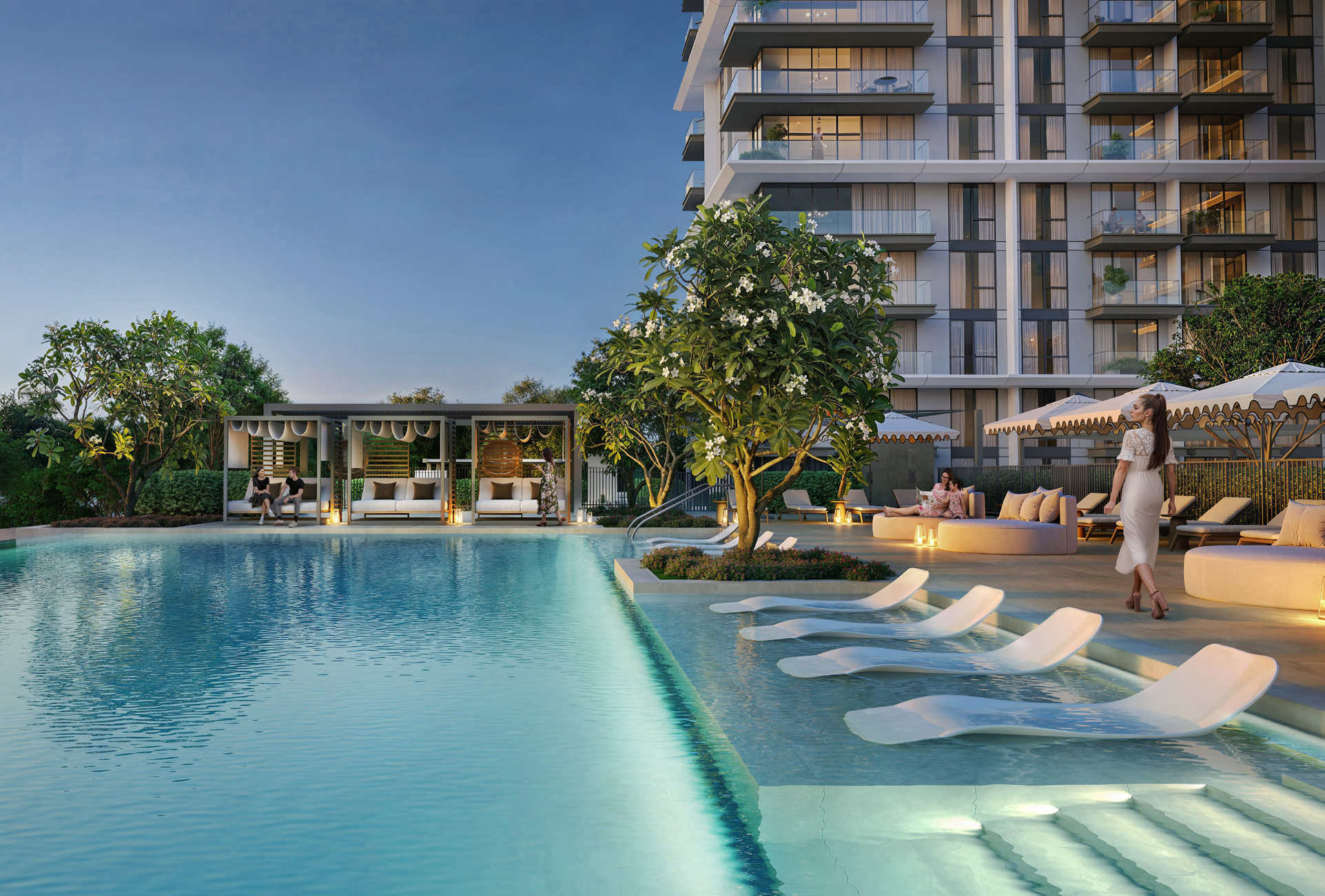 Pool at dusk with in-water loungers, cabanas and the residential tower behind
