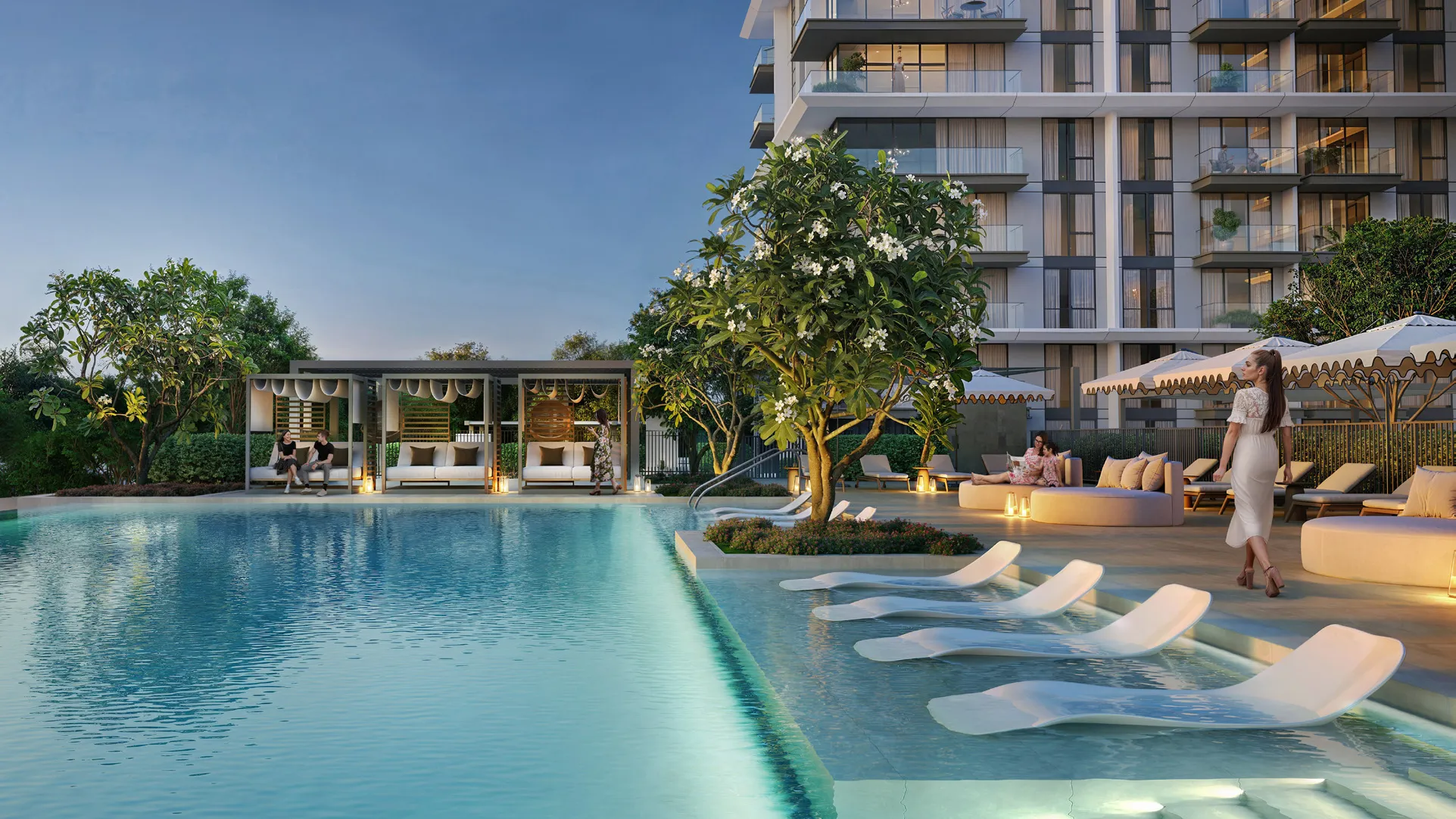 Pool at dusk with in-water loungers, cabanas and the residential tower behind