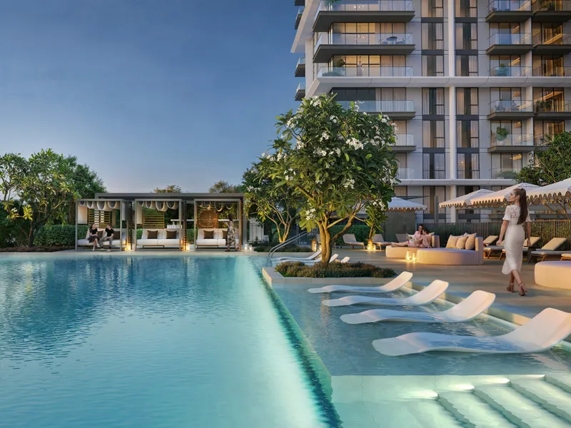 Pool at dusk with in-water loungers, cabanas and the residential tower behind