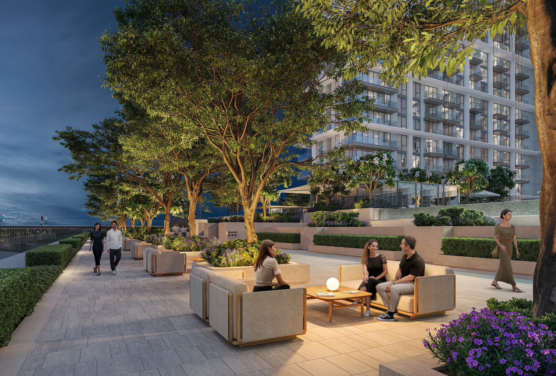 Podium deck with lounge seating beneath trees, towers lit behind