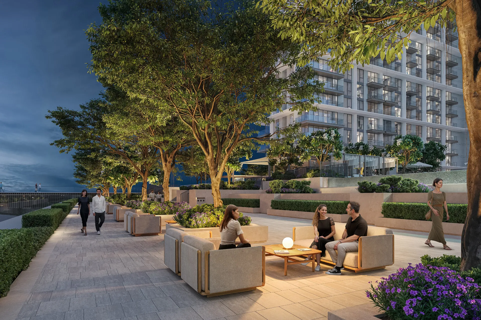 Podium deck with lounge seating beneath trees, towers lit behind