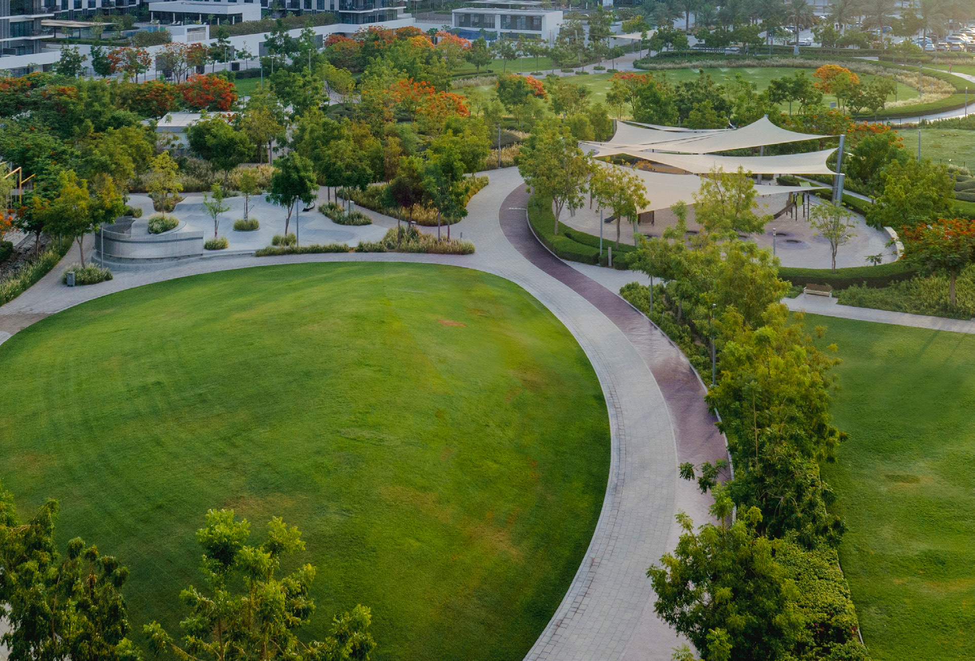Aerial view of Dubai Hills Park with lawns, paths and shaded play areas