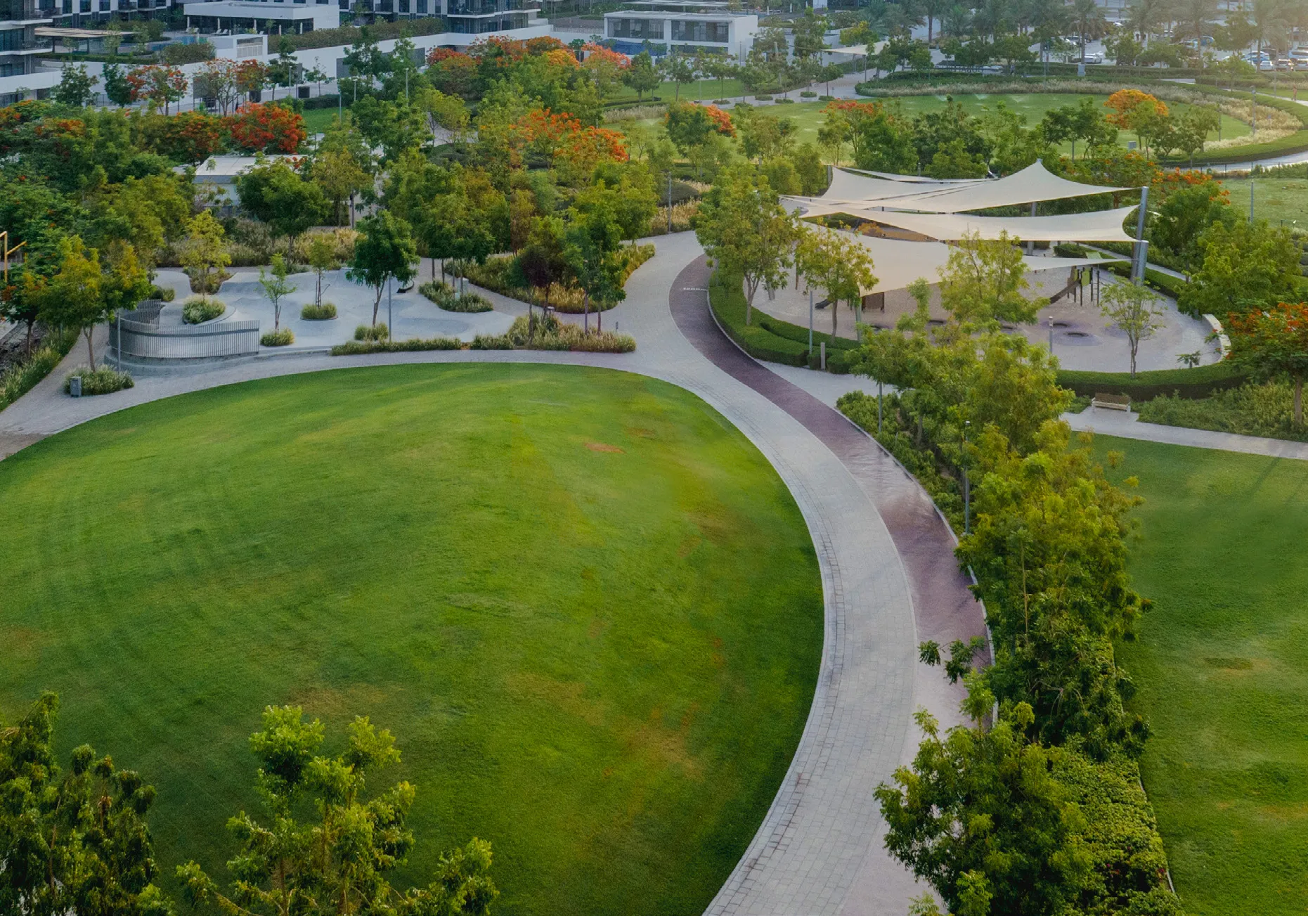 Aerial view of Dubai Hills Park with lawns, paths and shaded play areas