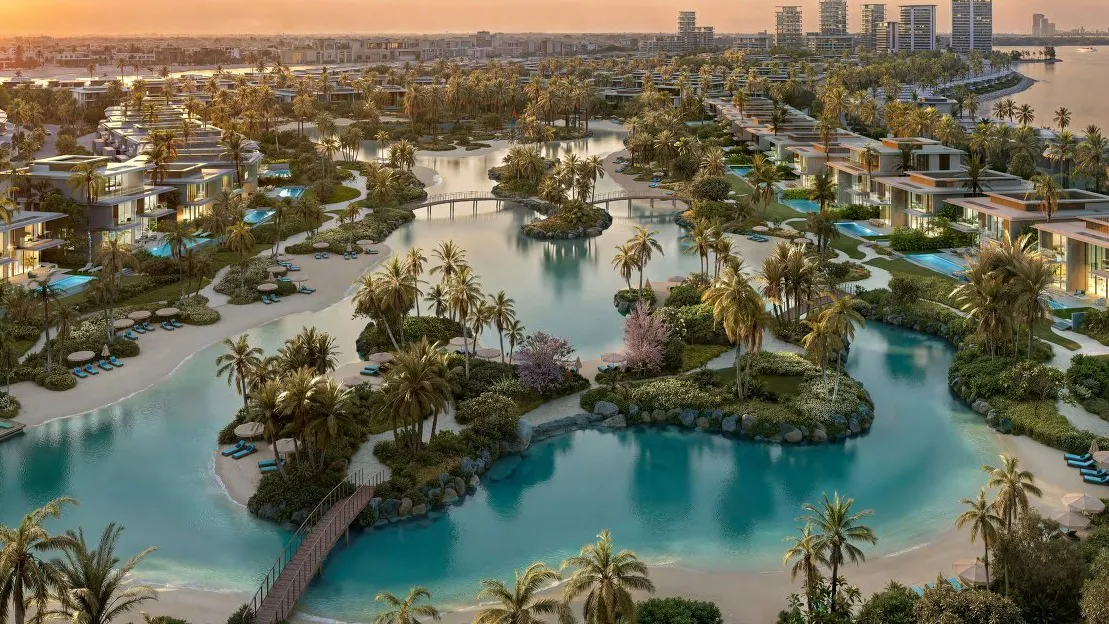Villas with private pools around a palm-lined swimmable lagoon at sunset